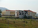 Eine ausgebrannte Schule, im Hintergrund der Neubau. (Bild öffnet sich in einem neuen Fenster)