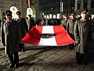 Sechs Angehörige der Einsatzorganisationen tragen die entfaltete Flagge. (Bild öffnet sich in einem neuen Fenster)