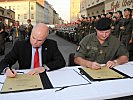 BAWAG PSK-Generaldirektor Byron Haynes, l., und der stellvertretende Wiener Militärkommandant, Oberst Gerhard Skalvy, unterzeichnen die Jubiläumsurkunde.