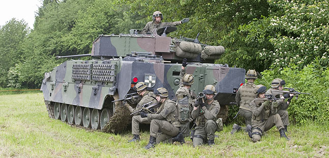 Soldaten knien hinter einem Schützenpanzer.