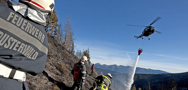 Ein Heereshubschrauber unterstützt die Feuerwehr bei einem Waldbrand in schwierigem Gelände.