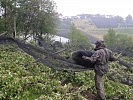 Ein Soldat errichtet über einer Obstplantage ein Hagelnetz.