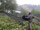 Ein Soldat errichtet über einer Obstplantage ein Hagelnetz.