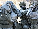 Unter gegenseitiger Hilfe legen die Soldaten die ABC-Schutzausrüstung an. (Bild öffnet sich in einem neuen Fenster)