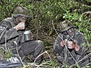 V.l.: Florian Gollob löffelt sein Mittagessen, während Magnus Gehrer mit dem Sturmgewehr sichert.