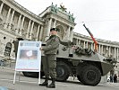 Wachtmeister Götz mit einer Info-Tafel. Im Hintergrund: Ein Radpanzer "Pandur".