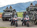 Zwei Militärpolizisten stehen mit ihren Motorrädern vor zwei Schützenpanzern.