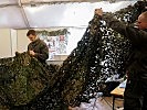 Letzte Handgriffe, wie hier mit einem Tarnnetz, werden im Zelt getätigt. (Bild öffnet sich in einem neuen Fenster)