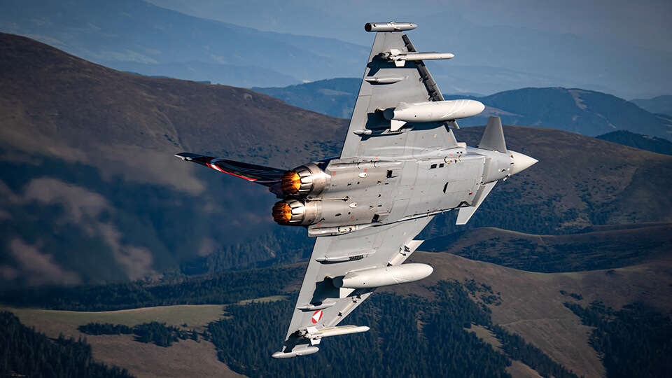 Kampfflugzeug Eurofighter EF 2000 des Österreichischen Bundesheereses fliegt zwischen dem Gebirge